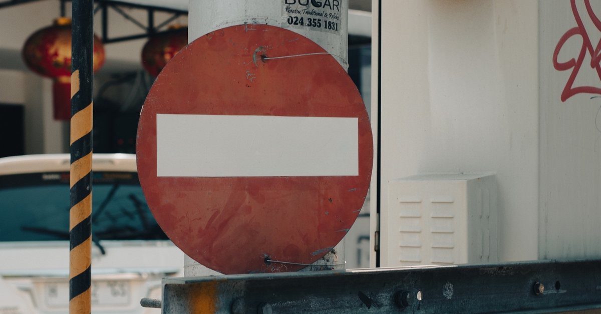 "No entry" road sign mounted on a pole in an urban setting with background elements including vehicles and hanging lanterns.