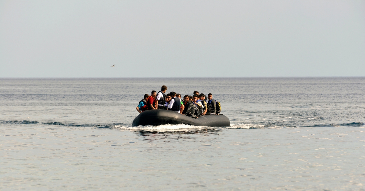 Group of people crossing calm sea waters in a crowded black inflatable boat.