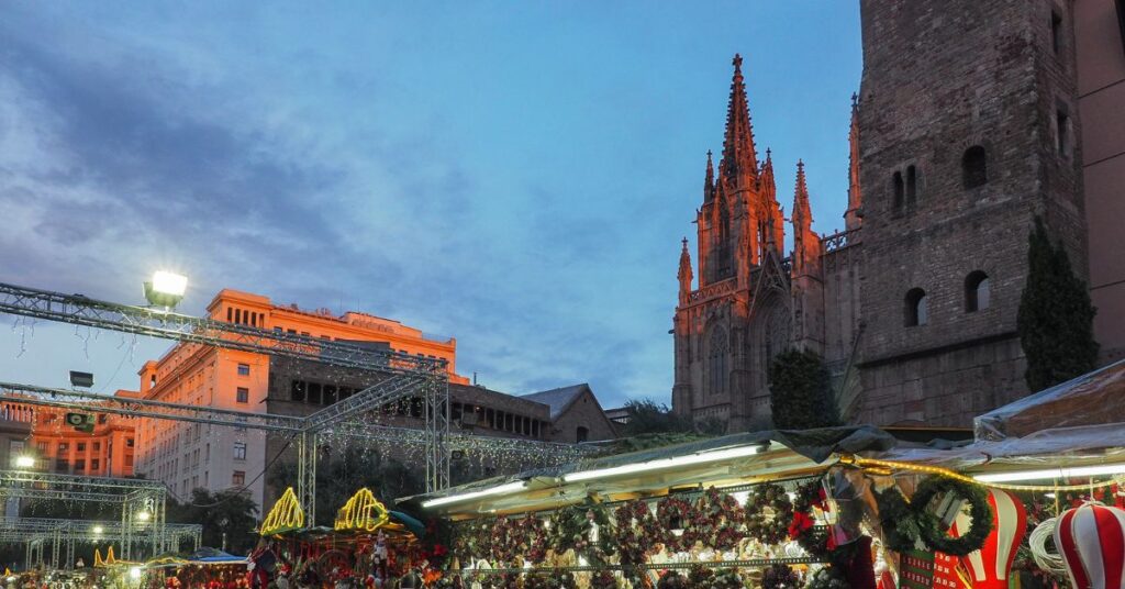 A crowded Christmas market with festive stalls in front of Barcelona Cathedral at dusk