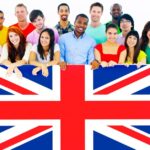 A diverse group of smiling people stand together holding a large Union Jack flag.