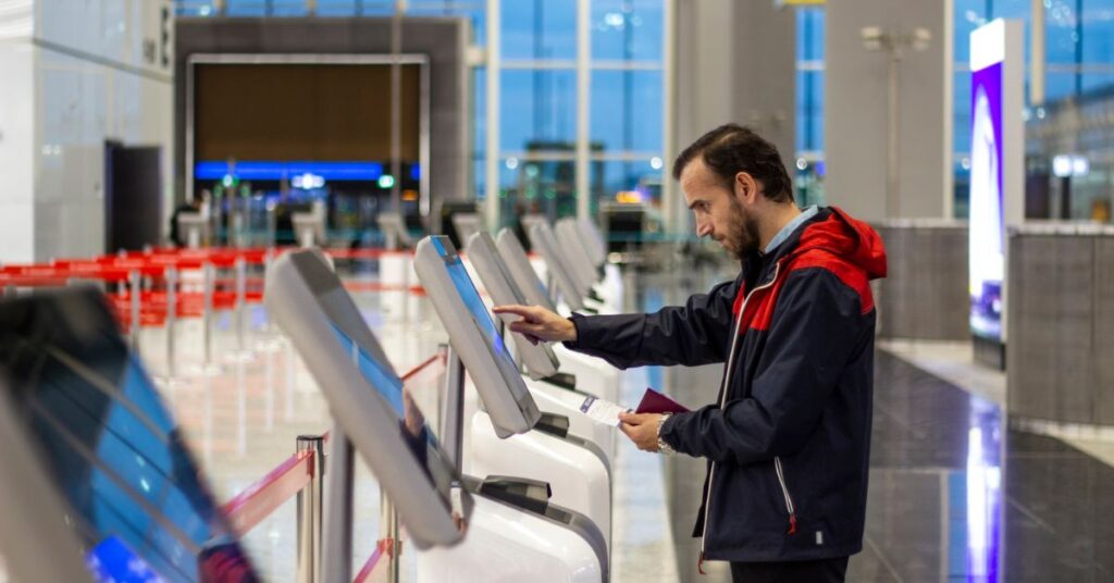 Man using a self-service check-in kiosk at an airport while holding his passport and ticket.