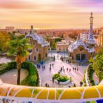 Colorful mosaic terrace overlooking Park Güell in Barcelona at sunset with Gaudí’s iconic buildings and city skyline.