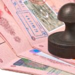 A stack of open passports with visa stamps and a black rubber stamp resting on top.