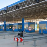 Empty border crossing checkpoint with blue booths and multiple closed lanes under a large metal canopy.