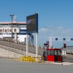 A ferry docked at the Calais port with an empty vehicle loading ramp under a clear blue sky.
