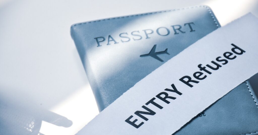 A passport partially covered by a paper strip that reads “ENTRY Refused” in bold letters.