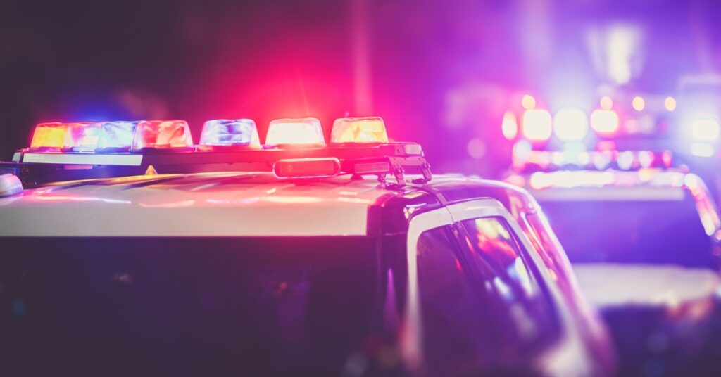 Police cars at night with red and blue lights flashing in a blurred, high-intensity urban scene.