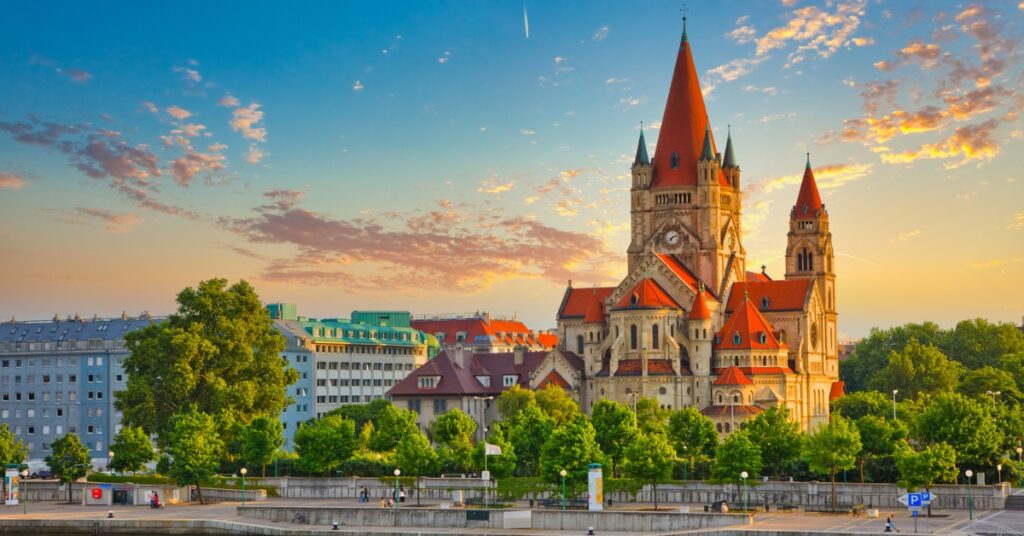 St. Francis of Assisi Church in Vienna stands along the Danube at sunset with warm light and a colorful sky.