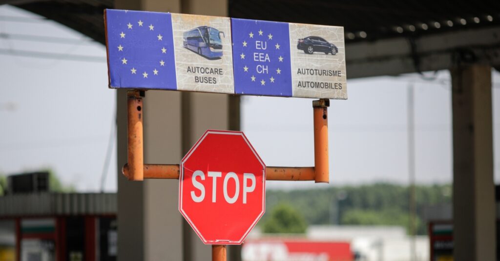 Stop sign at a European border checkpoint with EU signage indicating vehicle categories for buses and automobiles.