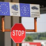Stop sign at a European border checkpoint with EU signage indicating vehicle categories for buses and automobiles.