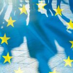 Silhouetted people walking on pavement with the European Union flag overlayed across the scene.