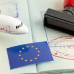 A toy airplane, EU flag, and stamp rest on an open passport showing visa markings on a world map background.