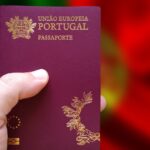 Hand holding a Portuguese passport against a blurred Portuguese flag background.