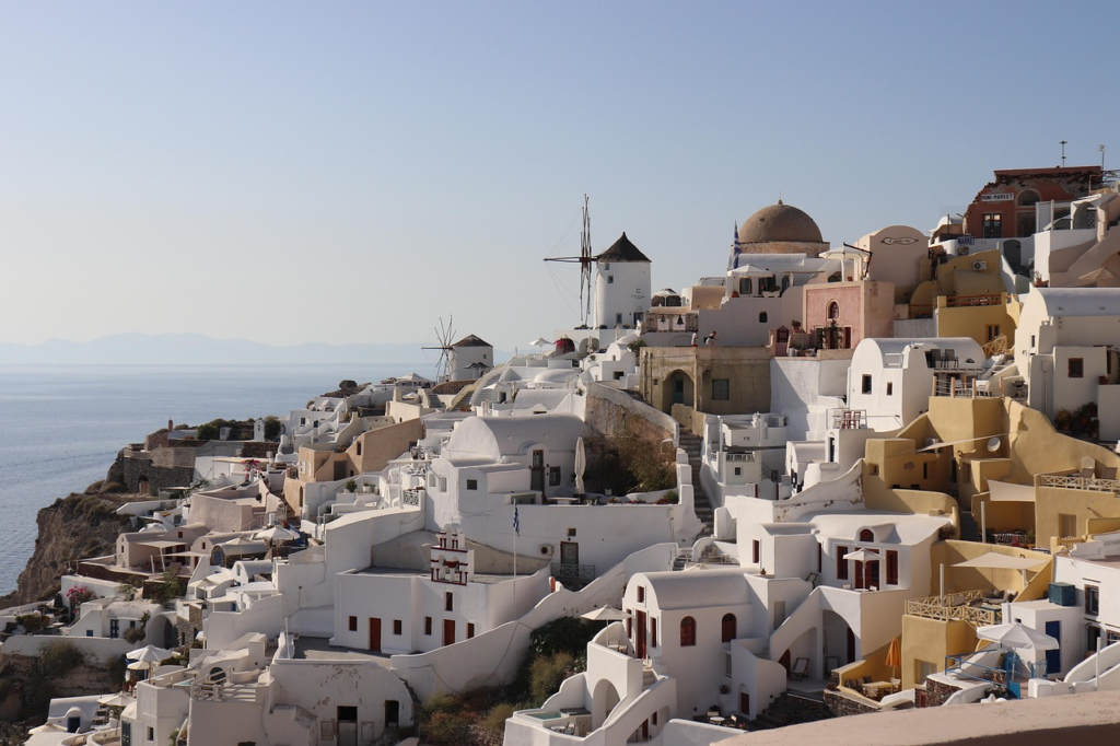 Cliffside village in Santorini with whitewashed houses and windmills overlooking the Aegean Sea under a clear sky.