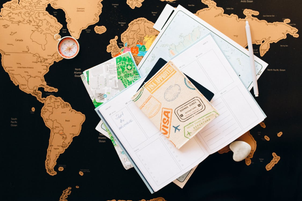 Flat lay of a passport, travel journal, maps, and a compass arranged on a world map, suggesting trip planning.