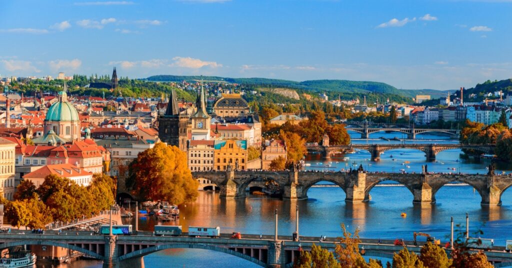 A panoramic view of Prague with historic bridges spanning the Vltava River and colorful buildings in the city center.