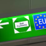 Green airport sign showing a left arrow, a “Zoll Customs” icon, and an EU symbol.