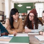 Group of college students sitting around a table, discussing notes and studying together in a library.