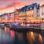 Colorful historic buildings and boats line a canal at sunset, with warm lights reflecting on the water.