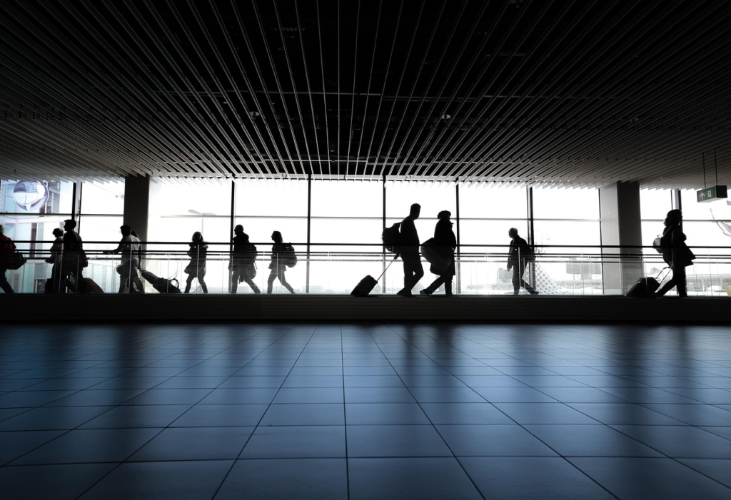 Silhouetted travelers walking through a modern airport terminal with large windows and carry-on luggage.