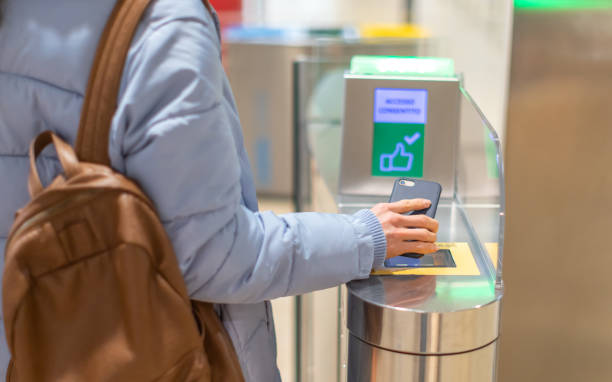 A person taps a smartphone on a contactless ticket gate while entering a transit station.