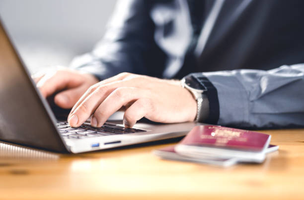 Hands typing on a laptop at a desk with a passport and smartphone placed nearby.