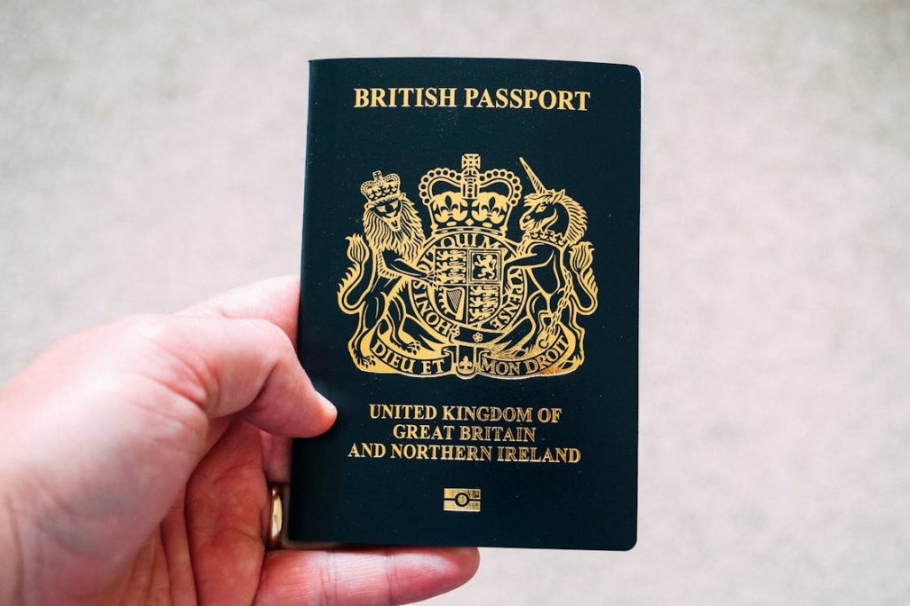 A hand holding a British passport showing the gold royal coat of arms on a dark cover.