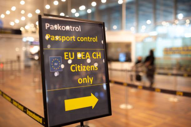 A passport control sign at an airport directs EU and EEA citizens, with travelers blurred in the background.
