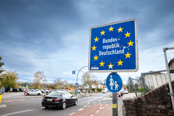 Germany border sign reading “Bundesrepublik Deutschland” with EU stars beside a road with passing cars.