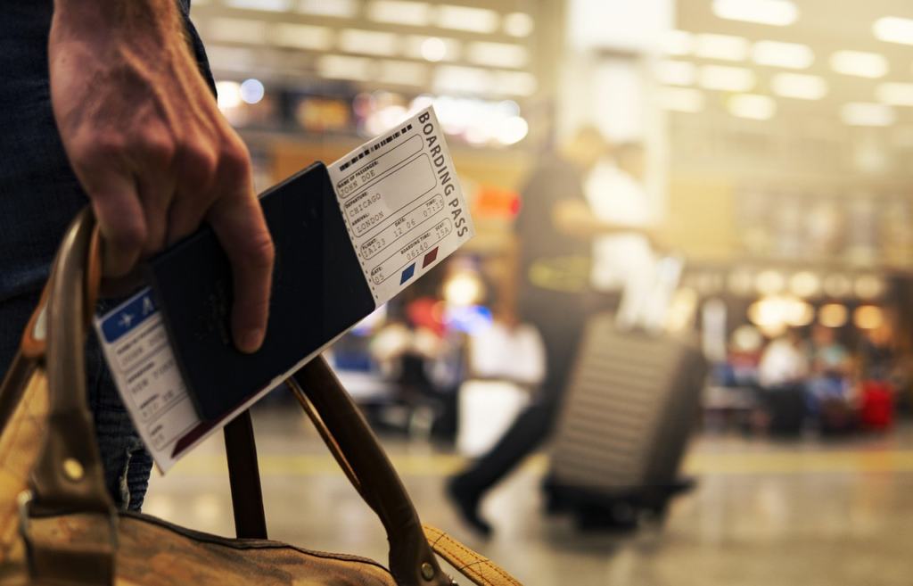Traveler holding a passport and boarding pass inside a busy airport terminal.