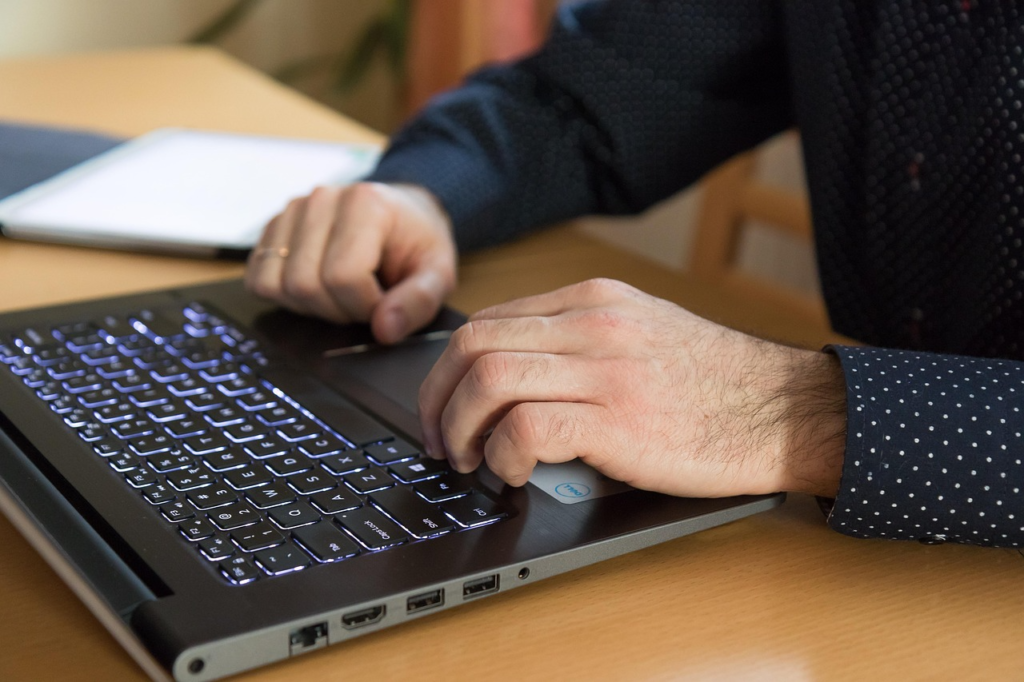 Person typing on a laptop keyboard while seated at a desk.