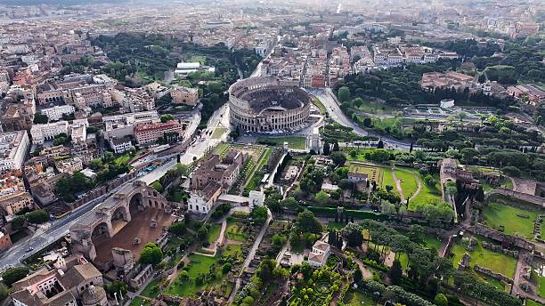 An aerial view of the Colosseum and surrounding Roman Forum, with historic ruins and green spaces spread across the city.