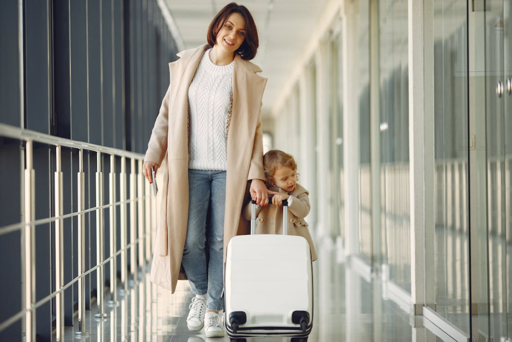 Woman and young child walking through an airport corridor while pulling a rolling suitcase.