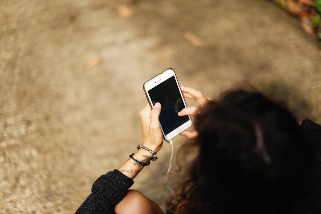 Person holding a smartphone while sitting outdoors, viewed from above with a blurred ground background.