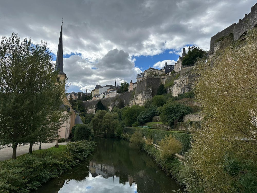 River flowing below historic hillside buildings and stone fortifications under a cloudy sky.