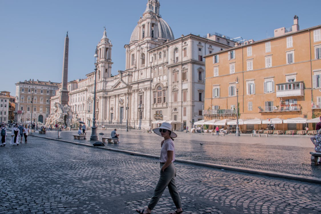 Wide view of Piazza Navona in Rome with a baroque church, obelisk fountain, and people walking across the square.