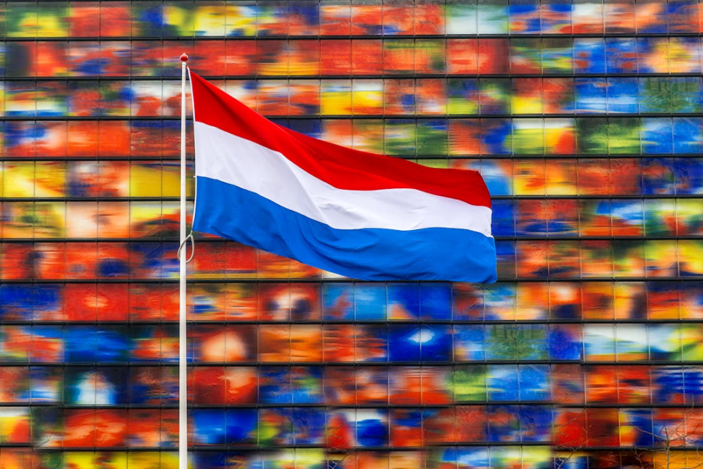 Dutch flag waving in front of a colorful glass building façade.