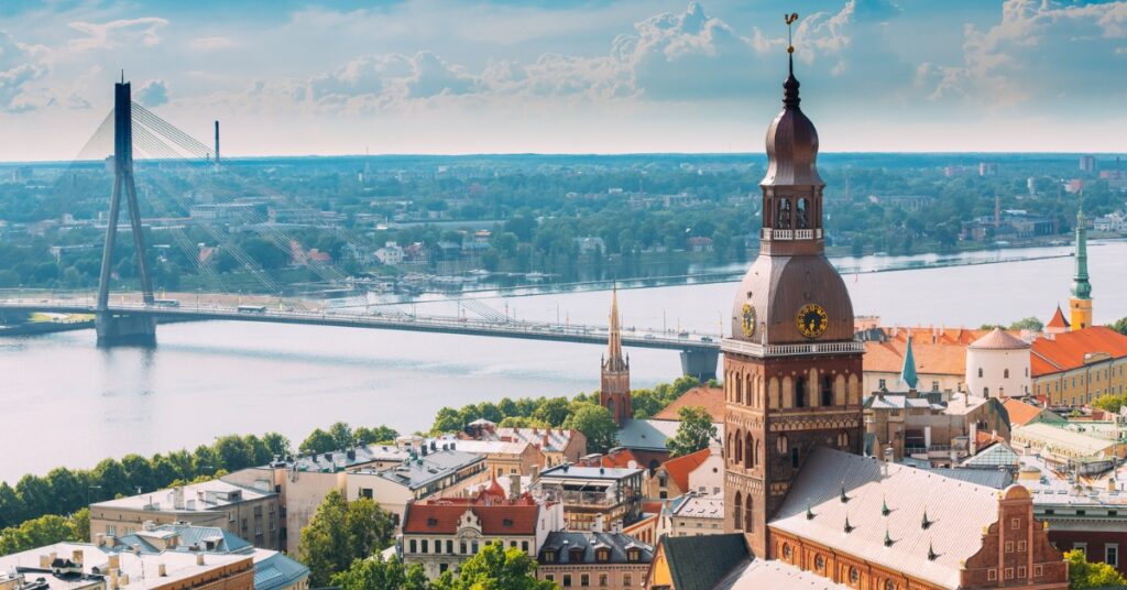 Cityscape of Riga Old Town with St. Peter's Church tower beside the Daugava River and a cable-stayed bridge.