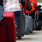 Travelers stand in a queue at an airport, lined up with rolling suitcases as they wait to proceed.