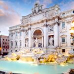 The Trevi Fountain in Rome glows at dusk, with baroque statues and flowing water framed by historic buildings.