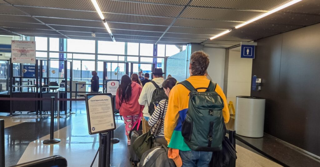 Travelers with backpacks and carry-on luggage waiting in an airport security line near gates.