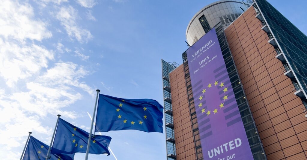 EU flags flying beside a parliament building with a “United for our Future 2024–2029” banner.