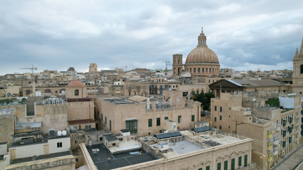 Historic city skyline with limestone buildings and a prominent domed church under an overcast sky.