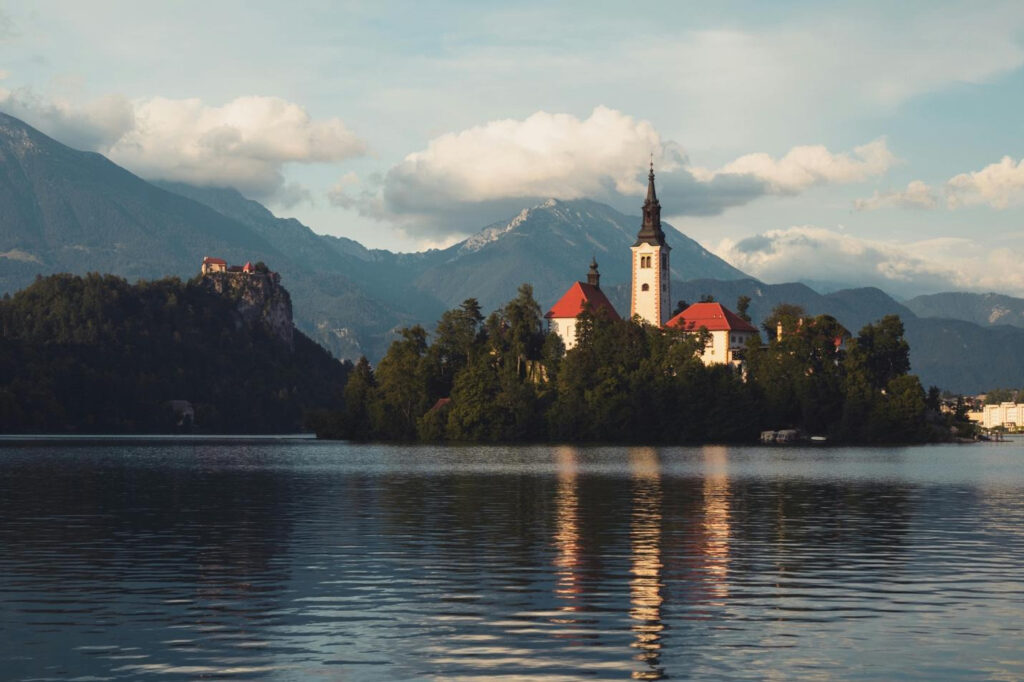 Church on a small island in a lake with mountains and clouds in the background.