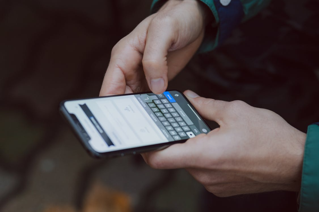 Hands holding a smartphone while typing on an onscreen keyboard, with the screen in focus against a blurred background.