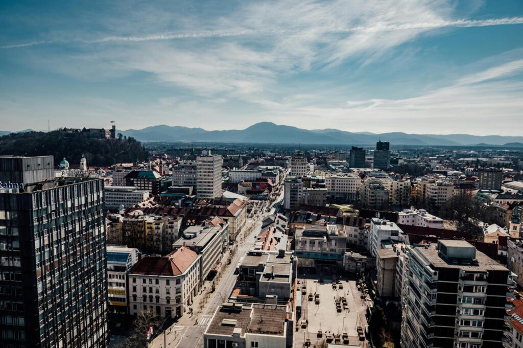 Aerial view of a cityscape with mountains in the background under a partly cloudy sky.