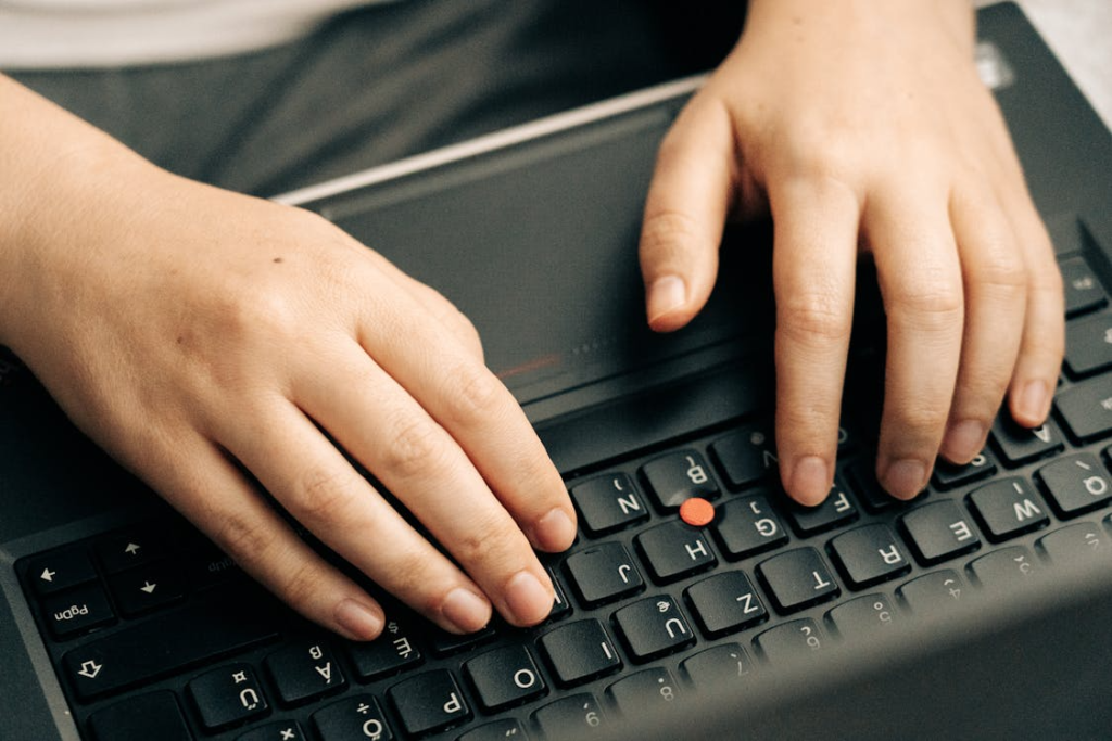 Close-up of hands typing on a laptop keyboard, with fingers positioned over the keys.