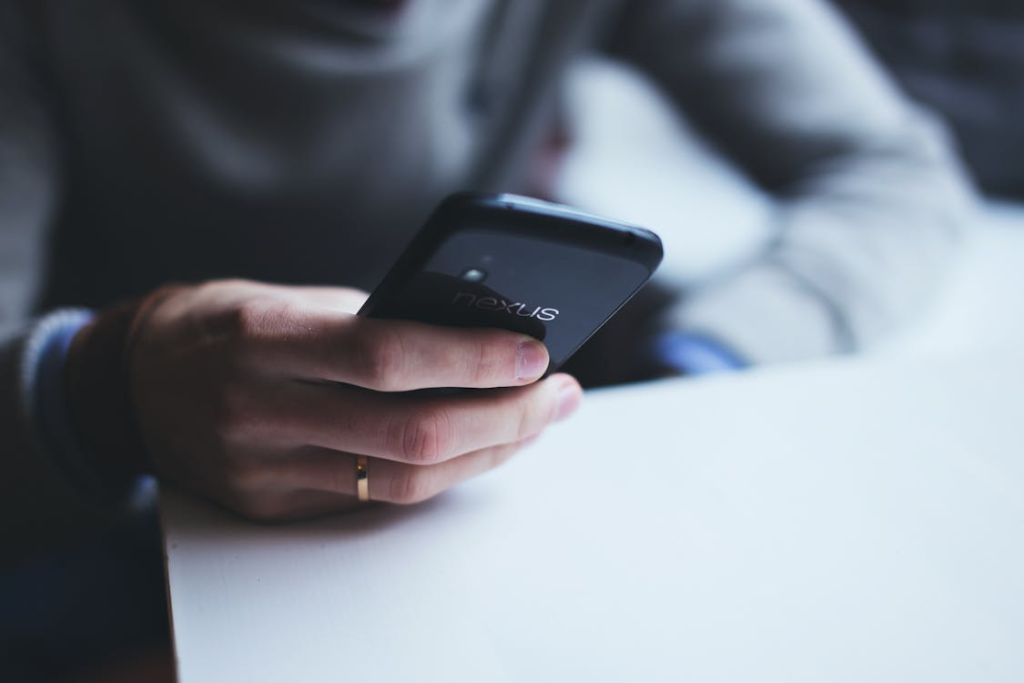Close-up of a hand holding a smartphone resting on a table, with the phone screen facing down.