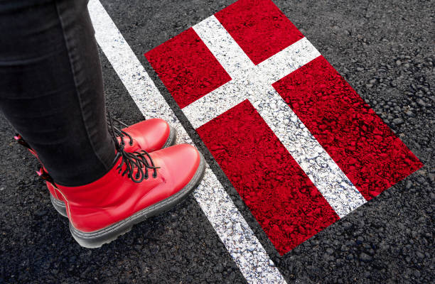 Red boots standing on a road marking painted like the Danish flag, with a white lane line beside it.