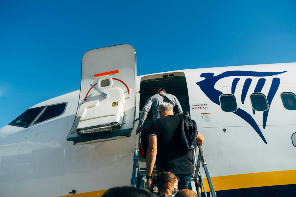 Passengers board a Ryanair airplane using outdoor stairs, with the aircraft door open against a clear blue sky.